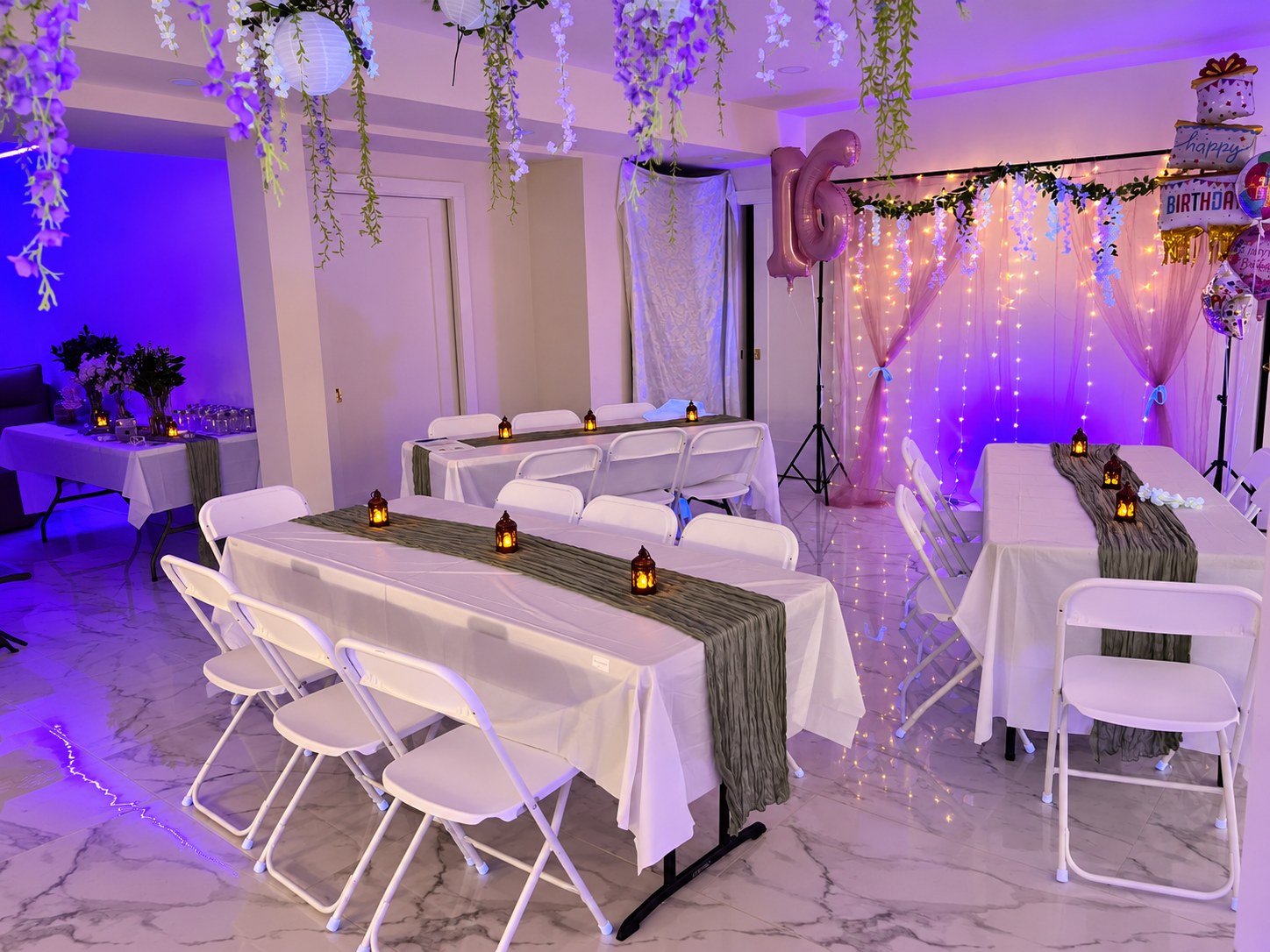White folding chairs around tables with white linens, green runners and small lantern decorations
