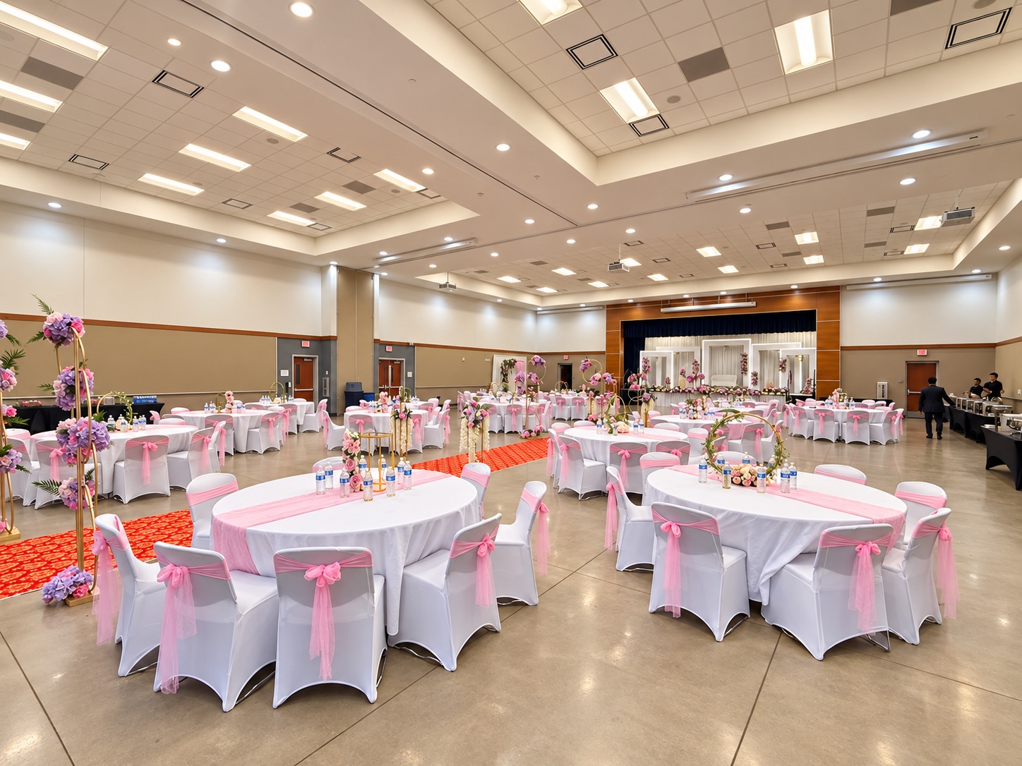 Pink and lavender indoor wedding reception with white-covered chairs, round tables and coordinated pink linens.