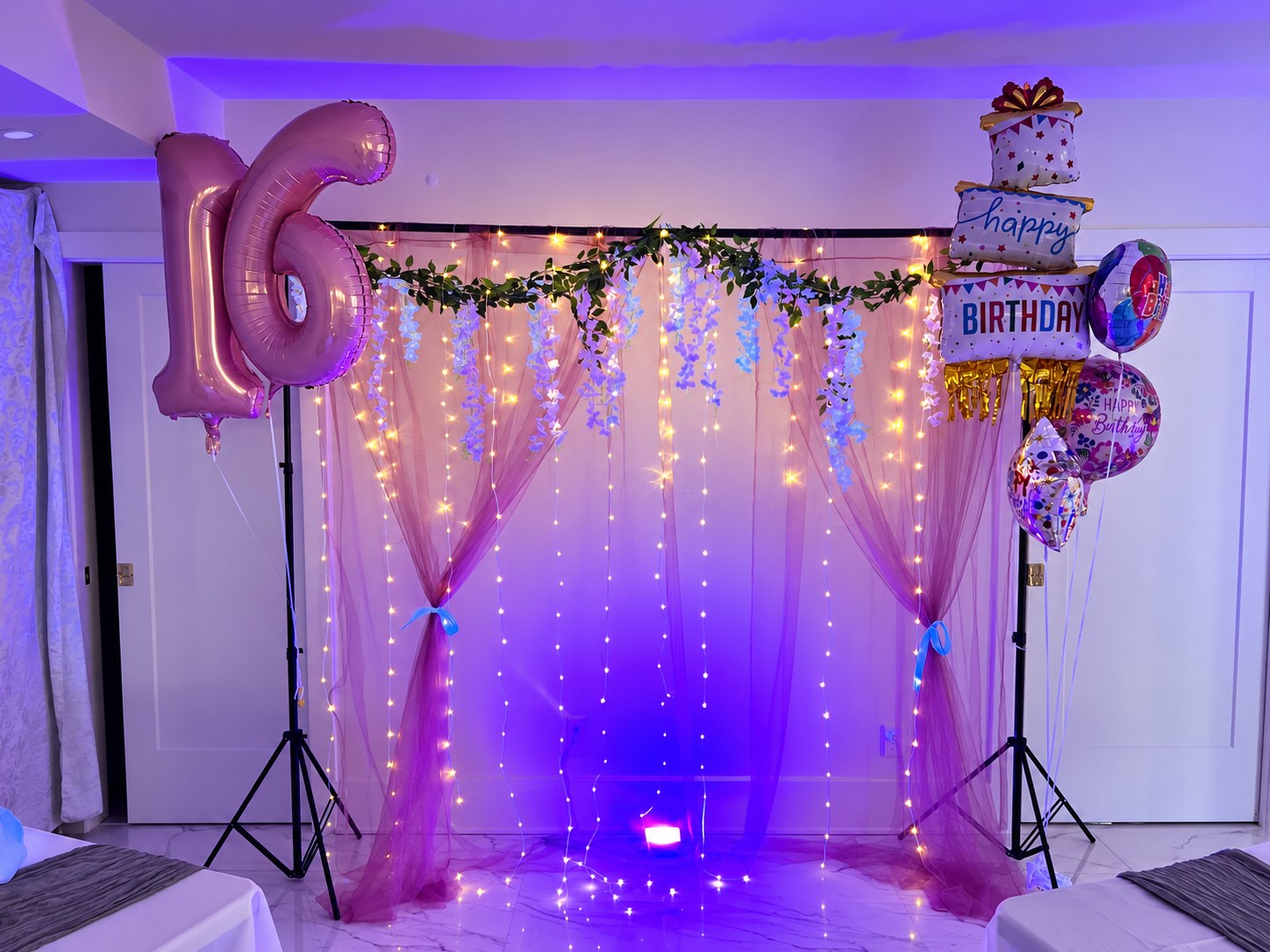Draped Sweet 16 backdrop with pink number balloons, hanging flowers and string lights
